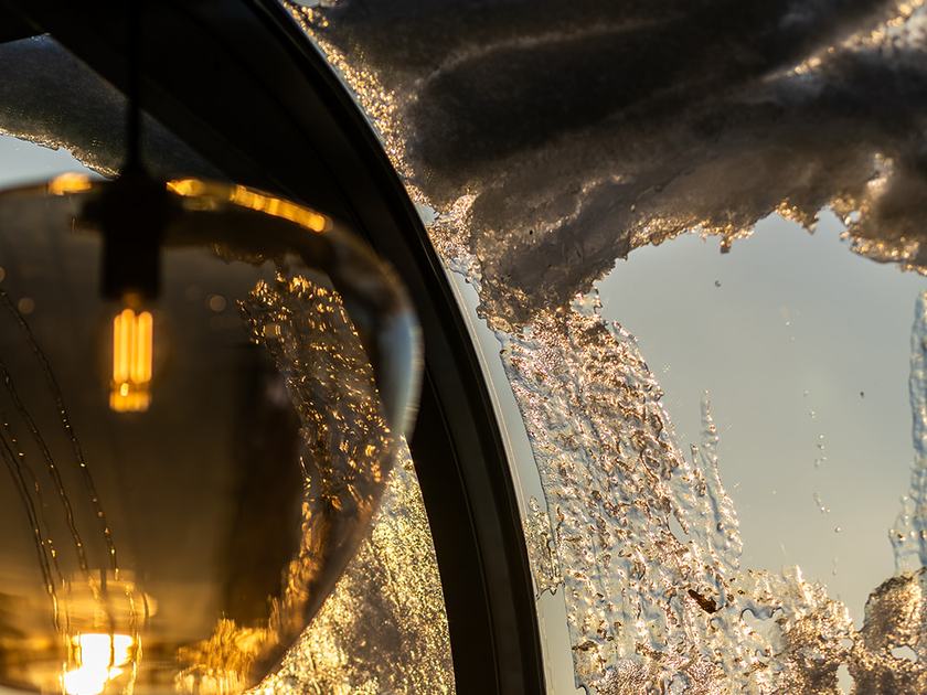 Pendellampe av gyllent glass foran et isete, buet vindu i vinterhagen på Strøm